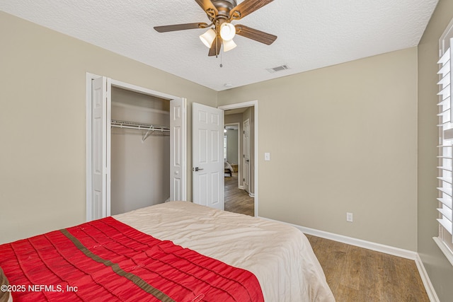bedroom with baseboards, a textured ceiling, wood finished floors, a closet, and ceiling fan
