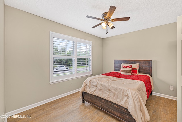 bedroom featuring wood finished floors, baseboards, a textured ceiling, and a ceiling fan