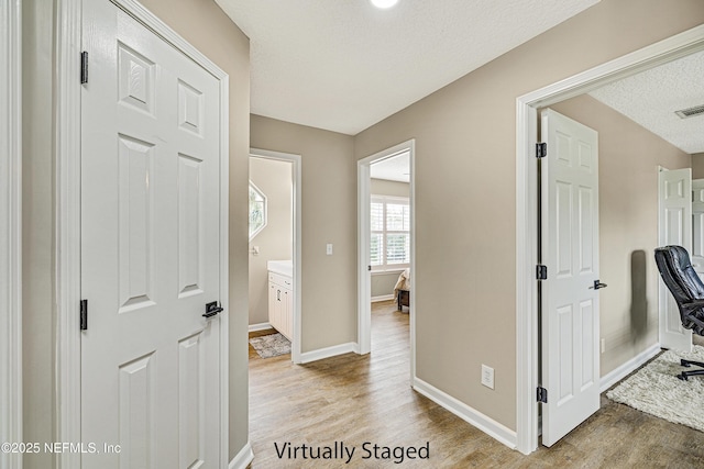 hall featuring wood finished floors, baseboards, and a textured ceiling