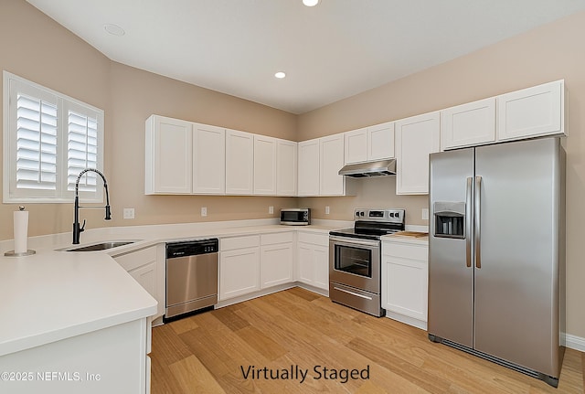 kitchen featuring appliances with stainless steel finishes, a sink, under cabinet range hood, light wood-style floors, and white cabinetry