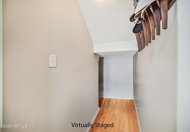 hall with a textured ceiling, baseboards, and wood finished floors
