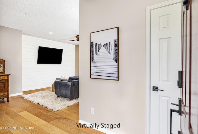 hall with wood finished floors, a textured ceiling, baseboards, and recessed lighting