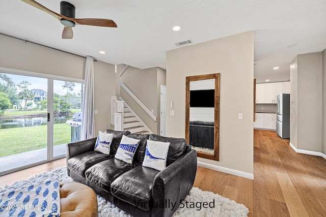 living area with light wood-style floors, stairs, a ceiling fan, a water view, and a textured ceiling