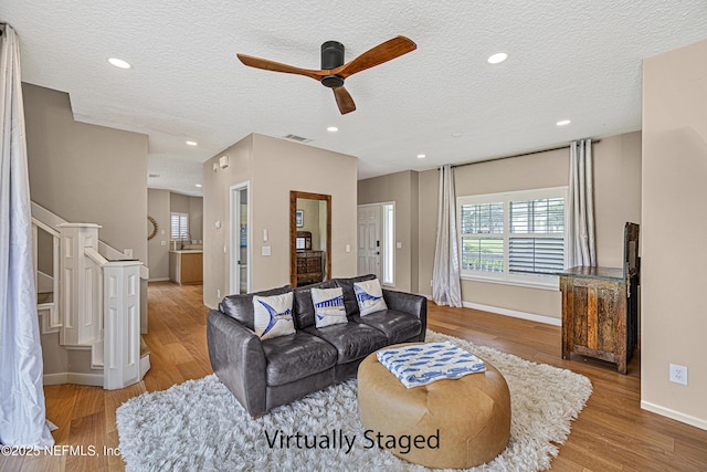 living room featuring stairs, ceiling fan, wood finished floors, a textured ceiling, and baseboards