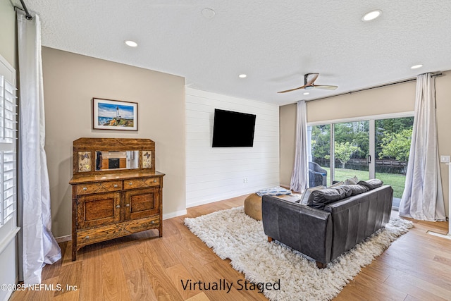 living area with a textured ceiling, ceiling fan, light wood finished floors, wood walls, and recessed lighting
