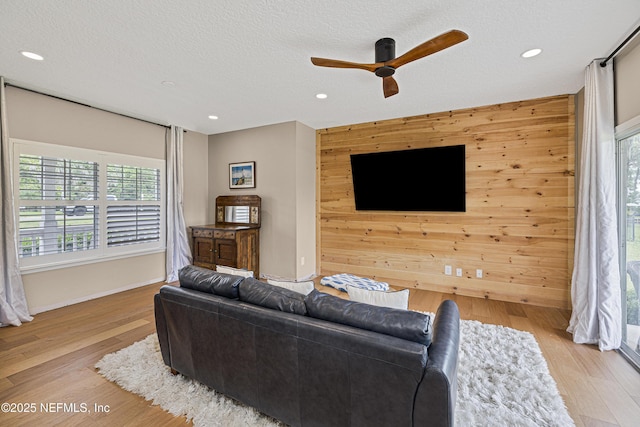 living room with wooden walls, ceiling fan, a textured ceiling, wood finished floors, and recessed lighting