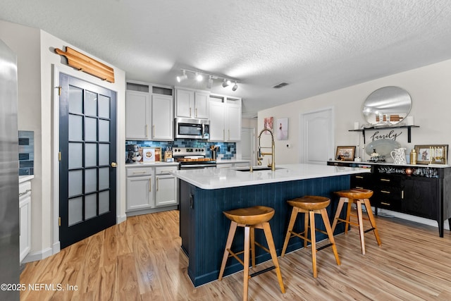4328 Packer Meadow Way, Middleburg, FL 32068 - kitchen featuring appliances with stainless steel finishes, a sink, a kitchen breakfast bar, light wood-type flooring, and light countertops