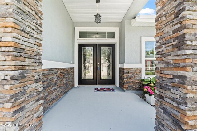 view of exterior entry with stone siding, french doors, and stucco siding