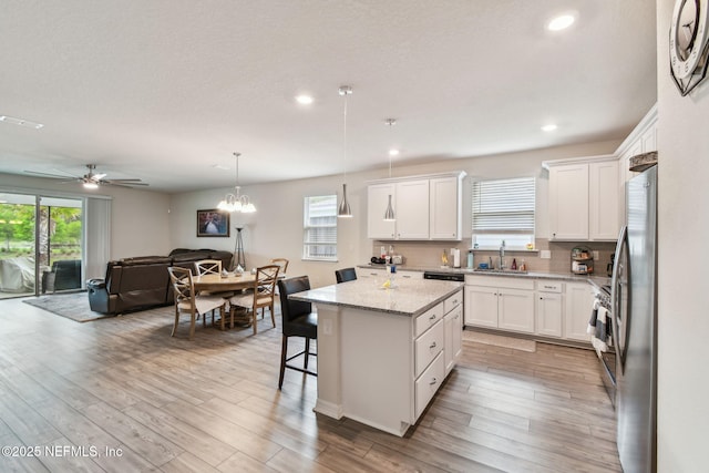kitchen with open floor plan, a center island, a sink, white cabinetry, and light wood-style floors