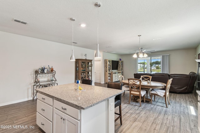 kitchen featuring open floor plan, light wood-type flooring, a kitchen island, white cabinets, and a kitchen breakfast bar