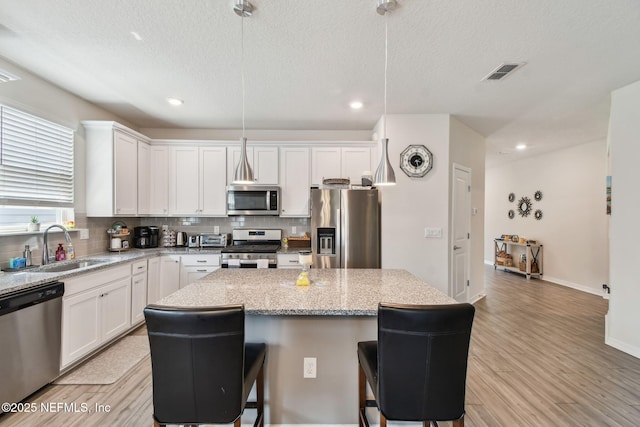 kitchen with stainless steel appliances, a sink, a center island, a kitchen bar, and tasteful backsplash