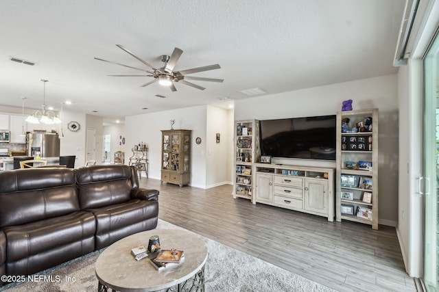 living area with a ceiling fan, wood finished floors, baseboards, a chandelier, and a textured ceiling