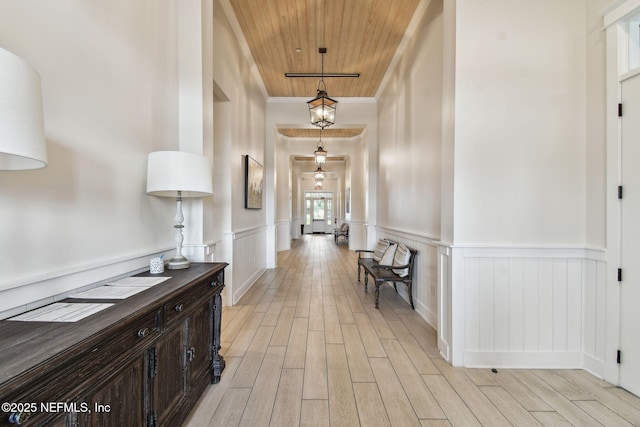 hallway featuring wooden ceiling, light wood-type flooring, a wainscoted wall, and crown molding
