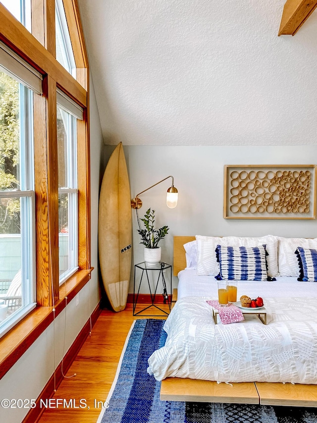 bedroom featuring a textured ceiling, wood finished floors, baseboards, and lofted ceiling