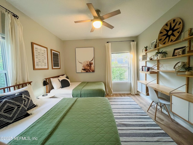 bedroom featuring wood finished floors, a desk, baseboards, and ceiling fan