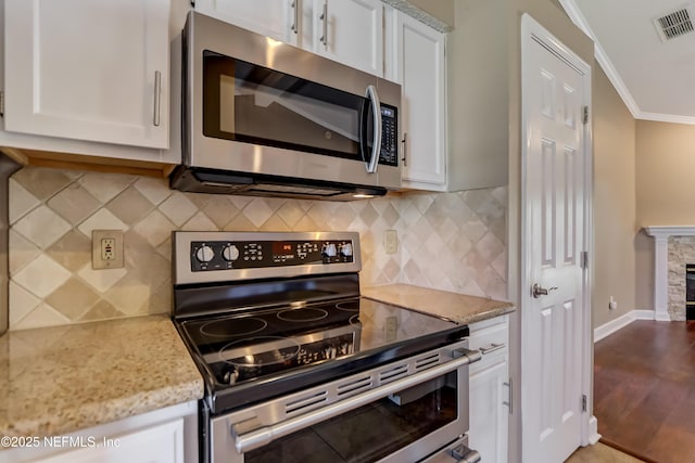 kitchen with appliances with stainless steel finishes, ornamental molding, white cabinets, and light stone countertops