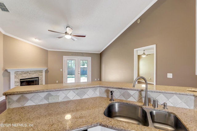 kitchen with a sink, a ceiling fan, light stone countertops, ornamental molding, and a stone fireplace