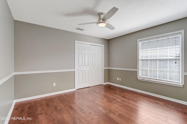 unfurnished bedroom with wood finished floors, a closet, a textured ceiling, baseboards, and ceiling fan