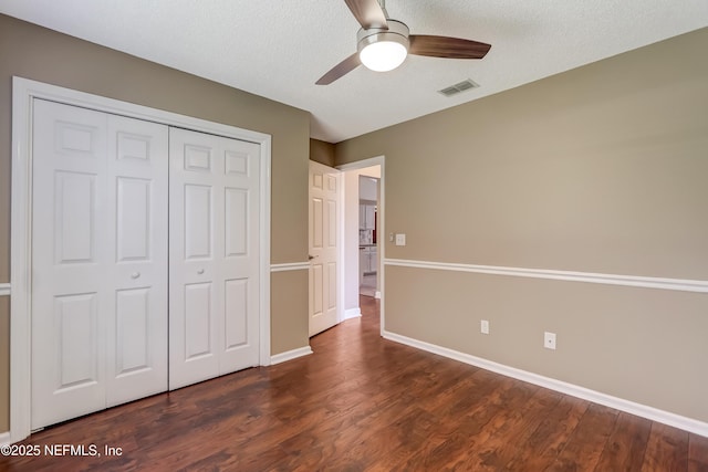 unfurnished bedroom featuring dark wood-style floors, a closet, baseboards, a ceiling fan, and a textured ceiling