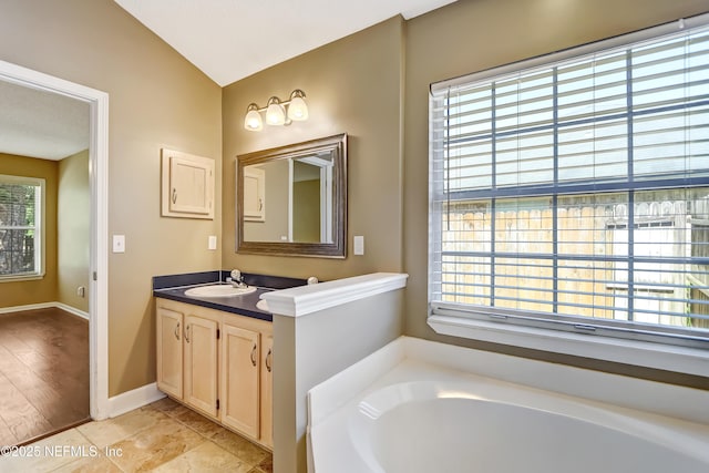full bathroom with a garden tub, vanity, vaulted ceiling, and baseboards