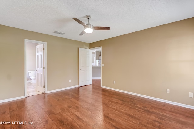 unfurnished bedroom with wood finished floors, a textured ceiling, baseboards, connected bathroom, and ceiling fan