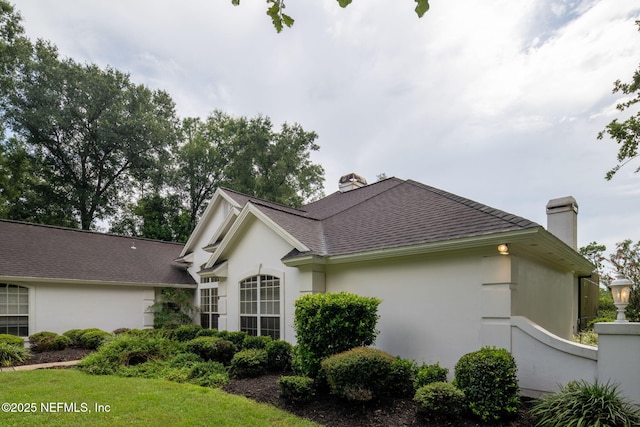 view of side of home featuring a chimney, stucco siding, a shingled roof, and a lawn
