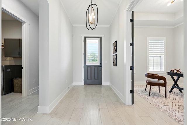 foyer with a chandelier, light wood-type flooring, baseboards, and ornamental molding