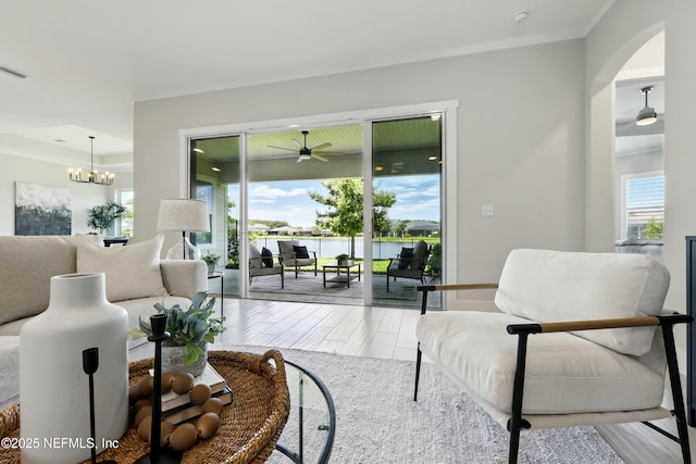 living room with a ceiling fan, arched walkways, a chandelier, and a water view