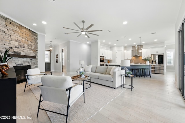 living room with ornamental molding, a stone fireplace, a ceiling fan, recessed lighting, and light wood-type flooring