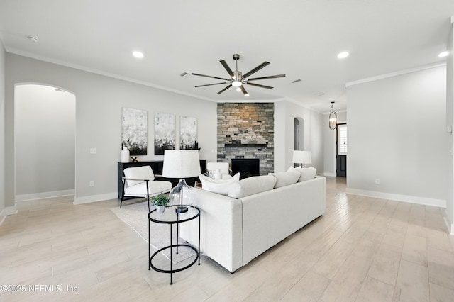 living room featuring arched walkways, ceiling fan, a fireplace, ornamental molding, and baseboards