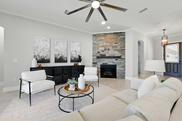 living room featuring ornamental molding, ceiling fan, arched walkways, light wood finished floors, and a stone fireplace