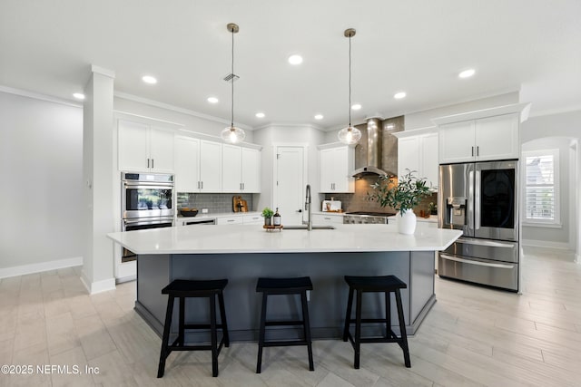 kitchen featuring wall chimney exhaust hood, appliances with stainless steel finishes, ornamental molding, a sink, and a large island