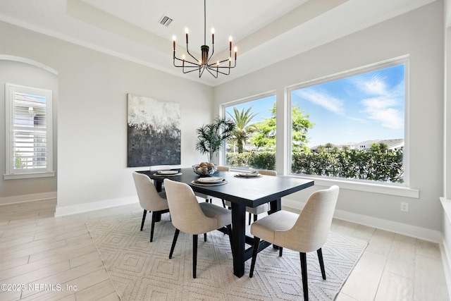 dining space with a chandelier, a raised ceiling, baseboards, and arched walkways