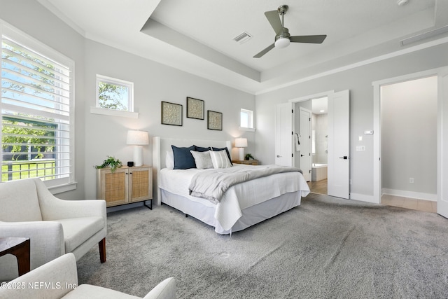 bedroom featuring carpet flooring, a tray ceiling, ensuite bathroom, ceiling fan, and baseboards