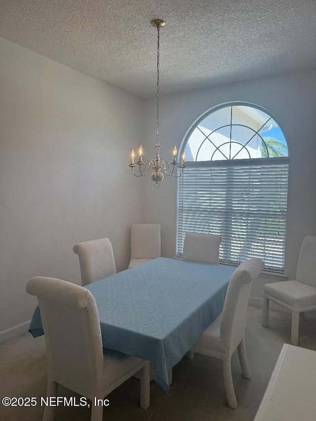 carpeted dining space with a textured ceiling, a chandelier, and baseboards