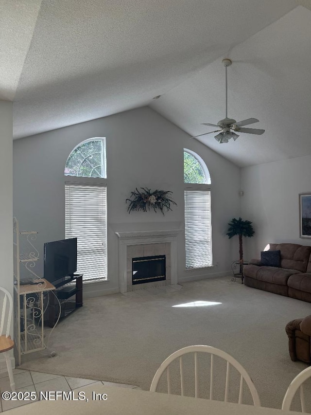 carpeted living room featuring a tiled fireplace, lofted ceiling, ceiling fan, and baseboards