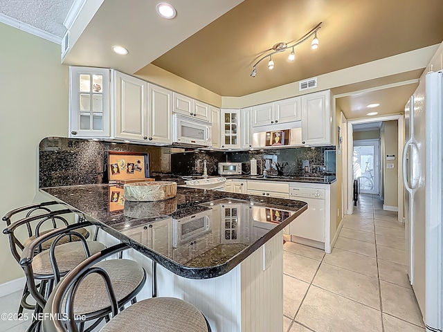 kitchen with white appliances, ornamental molding, a breakfast bar area, white cabinetry, and a peninsula