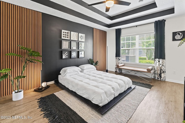 bedroom featuring wood finished floors, baseboards, a raised ceiling, and a ceiling fan