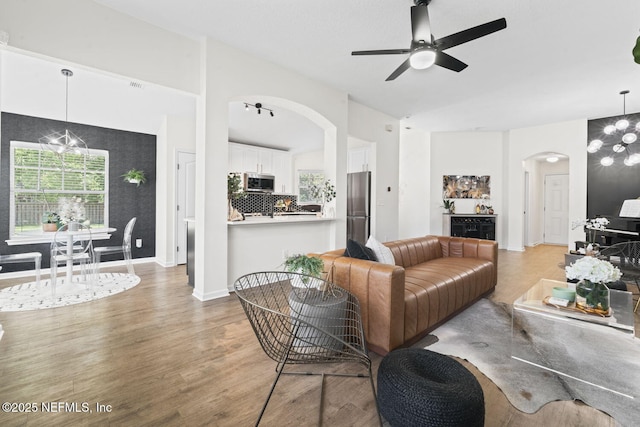 living area featuring arched walkways, light wood finished floors, a ceiling fan, baseboards, and vaulted ceiling