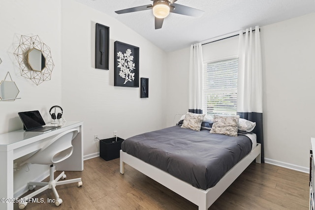 bedroom with wood finished floors, vaulted ceiling, an office area, a textured ceiling, and baseboards