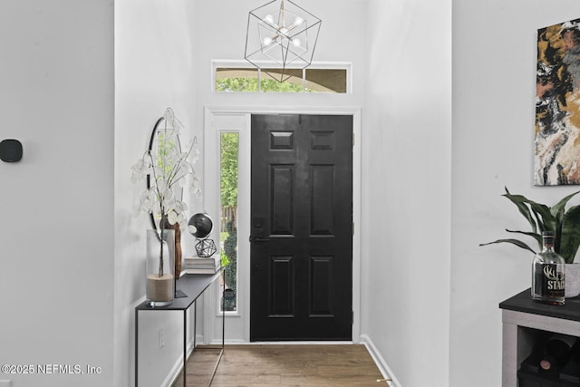 foyer with wood finished floors, a chandelier, baseboards, and a towering ceiling