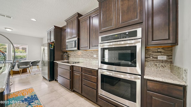 514 Heron Landing Rd, Saint Johns, FL 32259 - kitchen with appliances with stainless steel finishes, dark brown cabinetry, decorative backsplash, light tile patterned floors, and light stone counters