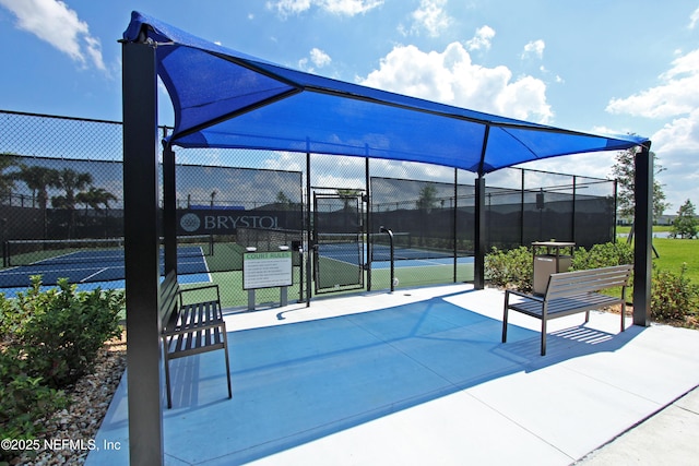 view of patio / terrace featuring a tennis court, fence, and a gate