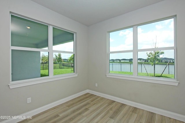 spare room with baseboards, a water view, and wood finished floors