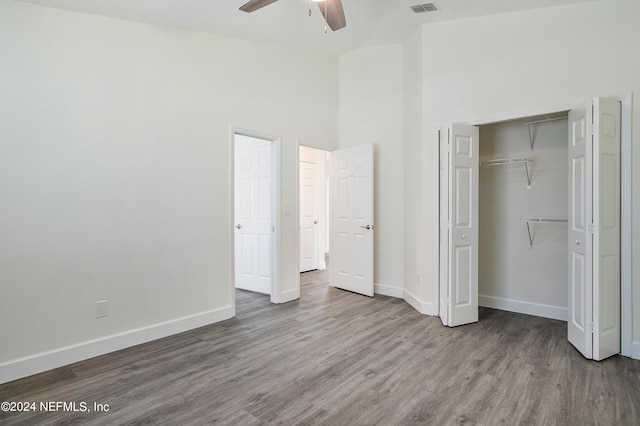 unfurnished bedroom with wood finished floors, baseboards, a closet, a ceiling fan, and high vaulted ceiling