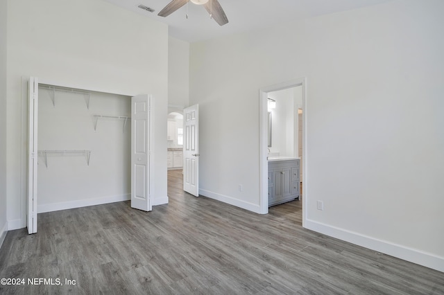 unfurnished bedroom featuring a closet, wood finished floors, arched walkways, baseboards, and high vaulted ceiling