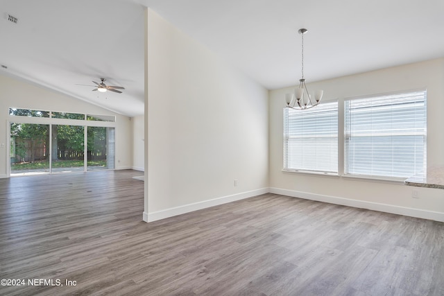 spare room with a chandelier, ceiling fan, plenty of natural light, lofted ceiling, and wood finished floors