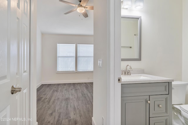 bathroom with toilet, wood finished floors, ceiling fan, vanity, and baseboards