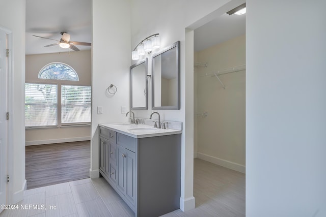 full bathroom featuring a ceiling fan, baseboards, double vanity, a walk in closet, and tile patterned floors