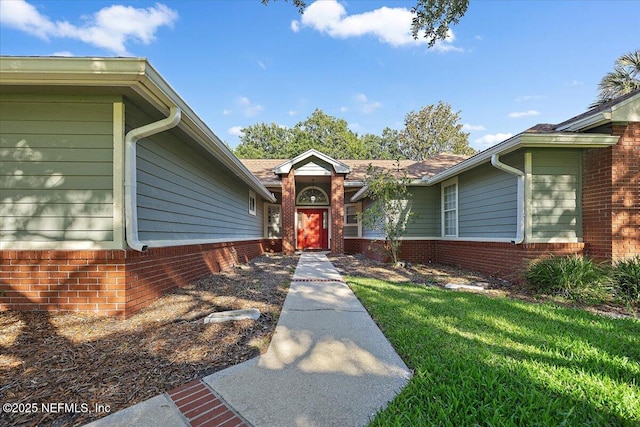 entrance to property featuring brick siding and a lawn